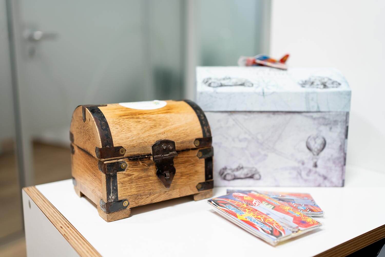Kleine hölzerne Schatztruhe auf einem Tisch, daneben bunte Hefte und eine dekorierte Geschenkbox